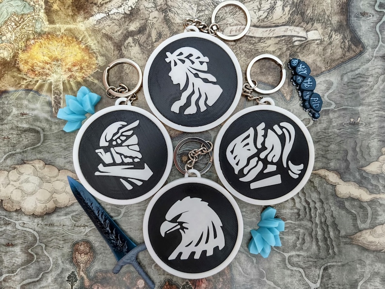 May include: A collection of black and white keychains with various graphic designs, including a profile, an eagle, and other stylized figures. Each keychain has a silver ring. Decorative blue objects and a blue sword are also present.