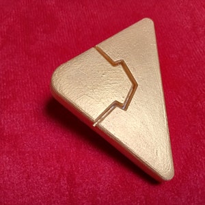 May include: A gold-colored triangular game piece with a raised, stylized arrow design.