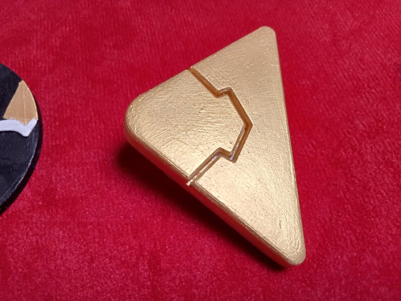 May include: A gold-colored triangular game piece with a raised, stylized arrow design.