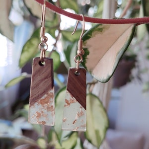 May include: A pair of gold dangle earrings with a rectangular wood and clear resin design. The resin is embedded with gold flakes.