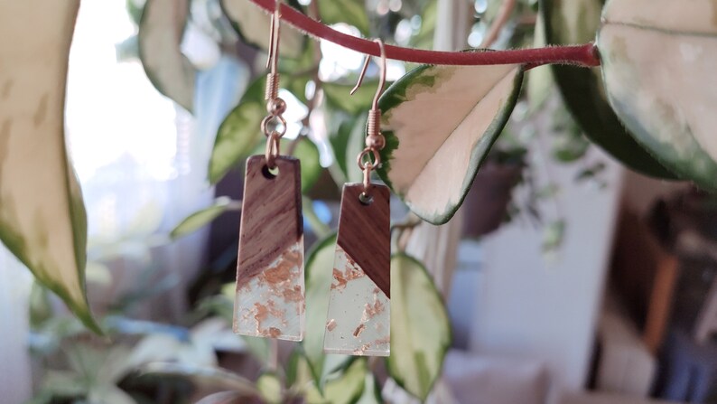 May include: A pair of gold dangle earrings with a rectangular wood and clear resin design. The resin is embedded with gold flakes.