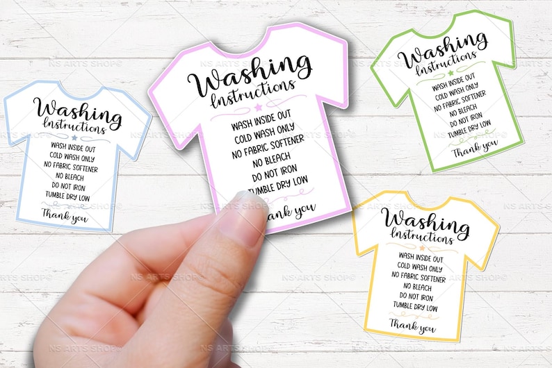 May include: A hand holding several t-shirt shaped washing instruction cards. Each card has the words "Washing Instructions" and laundry care details. The cards are outlined in blue, pink, green, and yellow.