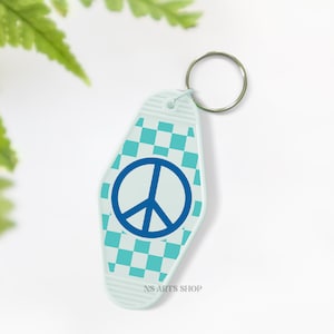 May include: A light blue motel-style keychain with a peace sign. The keychain has a checkered pattern in shades of blue and a silver key ring. The text "NS ARTS SHOP" is printed at the bottom of the keychain.