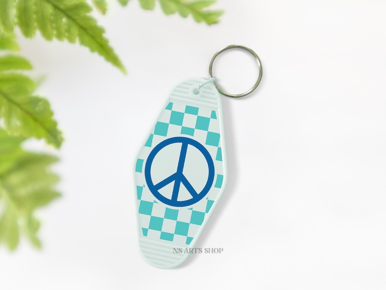 May include: A light blue motel-style keychain with a peace sign. The keychain has a checkered pattern in shades of blue and a silver key ring. The text "NS ARTS SHOP" is printed at the bottom of the keychain.