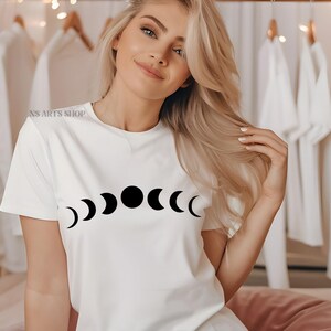 May include: A white t-shirt with a black moon phases design. The design features a full moon and crescent moons.