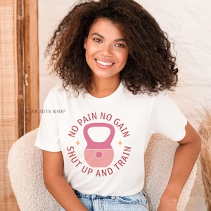 Puede incluir: Camiseta blanca con un gr&aacute;fico de pesa rusa rosa y blanca y el texto "No pain no gain shut up and train".