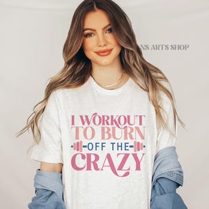 Puede incluir: Camiseta blanca con el texto "I workout to burn off the crazy" en letras rosas. El texto est&aacute; estilizado con un gr&aacute;fico de mancuerna rosa.