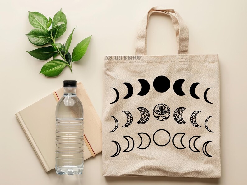 May include: A beige tote bag with black moon phases and a floral design. The bag has the text "NS ARTS SHOP" printed on the front.