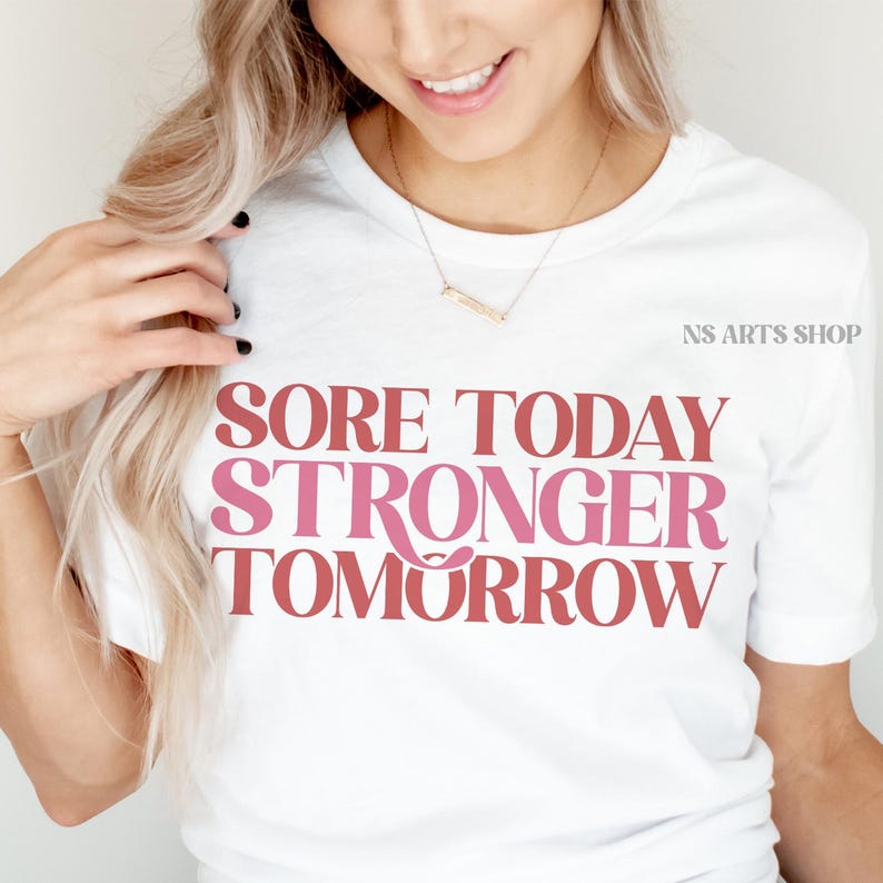 Puede incluir: Camiseta blanca con el texto "Sore Today Stronger Tomorrow" en letras rosa y rojo.