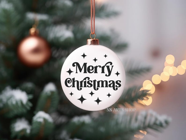 以下が含まれることがあります： 白いクリスマスオーナメントに黒い文字で「メリークリスマス」と書いてあり、黒い星形のアクセントが付けられています。