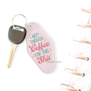 May include: A pink motel-style keychain with the text "NOT ENOUGH Coffee FOR THIS Shit" in pink and orange. A car key with a black head is attached. A planner and pen are in the background.