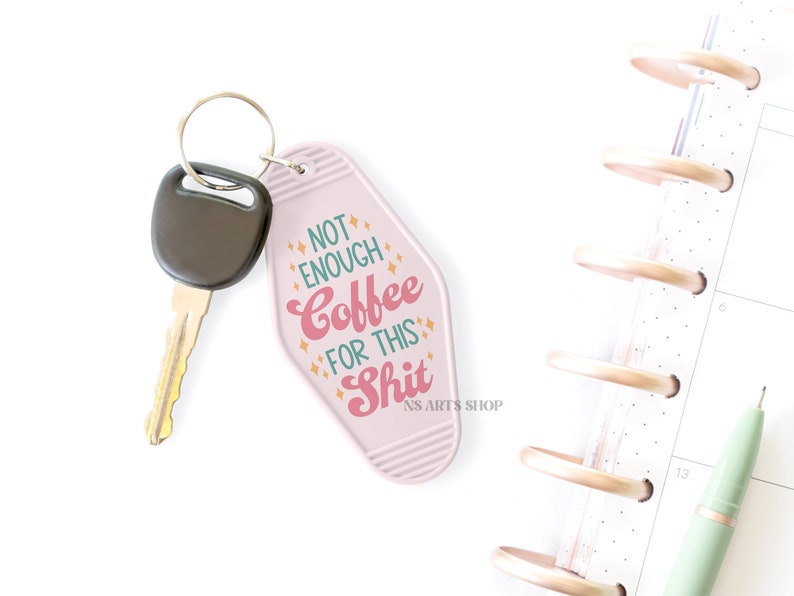 May include: A pink motel-style keychain with the text "NOT ENOUGH Coffee FOR THIS Shit" in pink and orange. A car key with a black head is attached. A planner and pen are in the background.