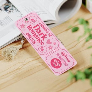 May include: A pink bookmark with the text "A Member of the Dark Romance Book Club" and skull and flower graphics. The bookmark has a tassel and the words "Lifetime Membership Admit One".