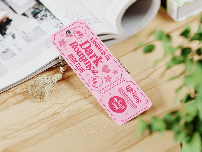 May include: A pink bookmark with the text "A Member of the Dark Romance Book Club" and skull and flower graphics. The bookmark has a tassel and the words "Lifetime Membership Admit One".