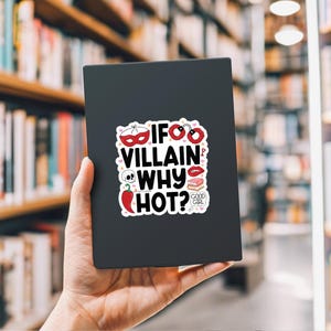 Puede incluir: Adhesivo negro con el texto "IF VILLAIN WHY HOT?" e ilustraciones variadas, incluyendo una m&aacute;scara, esposas, una calavera, un chile y un par de labios. El adhesivo se sostiene en una mano sobre un fondo borroso de estanter&iacute;as.