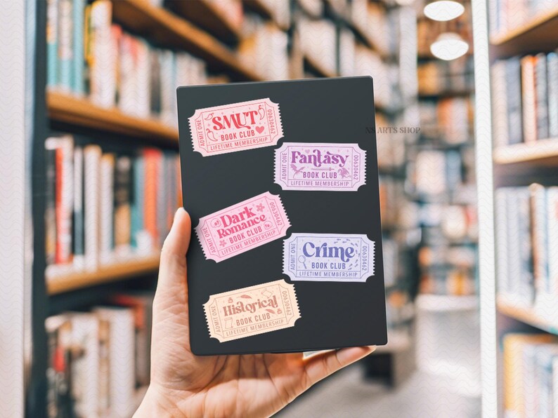 Puede incluir: Un objeto rectangular negro con cinco pegatinas coloridas en forma de boleto. Las pegatinas dicen "SMUT", "Fantasy", "Dark Romance", "Crime" e "Historical" con el texto "Book Club" y "Lifetime Membership".