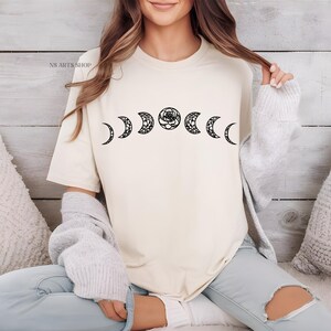 May include: A white t-shirt with a black graphic of a crescent moon and a rose. The graphic is repeated across the shirt, creating a pattern of six moons and roses.