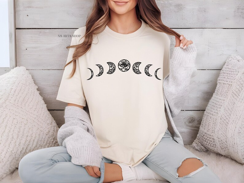 May include: A white t-shirt with a black graphic of a crescent moon and a rose. The graphic is repeated across the shirt, creating a pattern of six moons and roses.