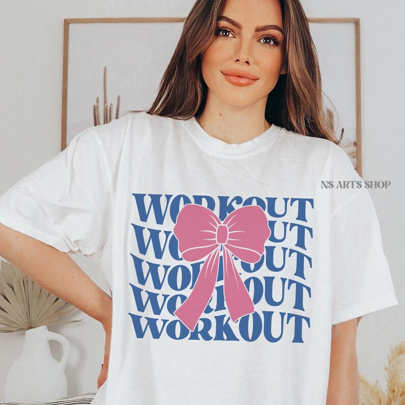 Puede incluir: Camiseta blanca con la palabra "WORKOUT" repetida cinco veces en texto azul. Un lazo rosa est&aacute; centrado en la camiseta.