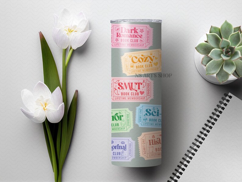 Puede incluir: Un vaso gris con dise&ntilde;os de boletos coloridos para varios clubes de lectura, incluyendo "Dark Romance", "Cozy" y "Smut". El vaso est&aacute; decorado con detalles florales y el texto "NS ARTS SHOP".