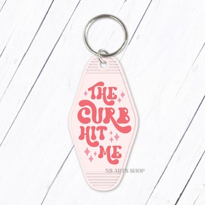 May include: A pink motel-style keychain with the phrase "THE CURB HIT ME" in red retro font. The keychain has a silver key ring and the text "NS ARTS SHOP" at the bottom.