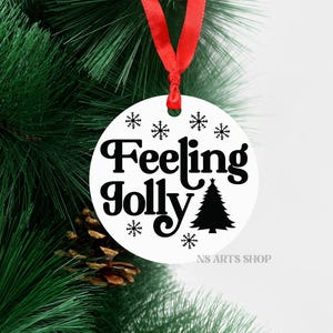 以下が含まれることがあります： 黒い文字で「Feeling Jolly」と書いてある白い丸いクリスマスオーナメント。クリスマスツリーの黒いシルエットと、黒い雪の結晶が文字の周りにあります。