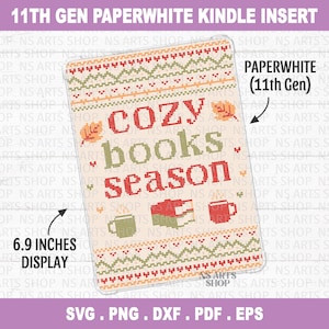 May include: A rectangular insert for an 11th Gen Paperwhite Kindle with a 6.9 inch display. The design features a cross-stitch pattern with the text "cozy books season" in red and green, surrounded by autumn leaves, a book, and two mugs.