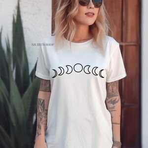 May include: White t-shirt with a black graphic of a moon phase cycle. The graphic shows the moon in different phases, from a crescent to a full moon.