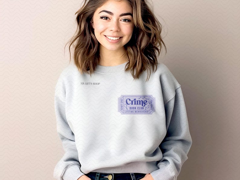 Puede incluir: Sudadera gris claro con el texto "Crime Book Club" impreso en un dise&ntilde;o de boleto morado. La sudadera tambi&eacute;n tiene el texto "NS Arts Shop" impreso en la parte superior izquierda.