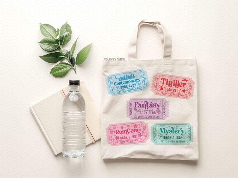 Puede incluir: Una bolsa de mano blanca con dise&ntilde;os de boletos de club de lectura coloridos. Los boletos est&aacute;n etiquetados como "Contemporary", "Thriller", "Fantasy", "RomCom" y "Mystery". Una botella de agua y un cuaderno est&aacute;n junto a la bolsa.