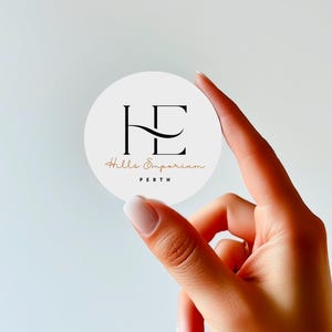 May include: A circular white sticker featuring a black logo with the letters HE, with the text Hills Emporium in a cursive copper font and the word PERTH in black capital letters underneath, presented on a plain light background.