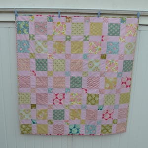May include: A pink and green patchwork quilt with a variety of floral and geometric patterns. The quilt is made up of many small squares sewn together.