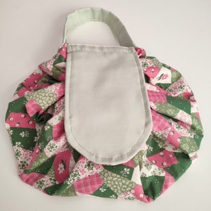 May include: A green and pink floral print drawstring bag with a light green fabric pocket and a light green handle.