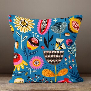 May include: Square throw pillow with a vibrant floral pattern in shades of yellow, pink, and brown on a teal background. The design includes stylized flowers, insects, and geometric shapes. The pillow is placed on a wooden surface.