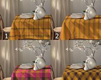 May include: Four different plaid tablecloths in shades of yellow, pink, and brown are displayed on tables. Each table is set with white plates, a white vase with flowers, and a smaller white vase. The tablecloths have different plaid patterns.