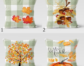 Op de afbeelding: Vier decoratieve sierkussens met herfstthema's. Elk kussen heeft een groen-wit geruit patroon. Ontwerpen omvatten herfstbladeren, eikels, een boom met herfstbladeren en een pompoen met de woorden "hello fall".