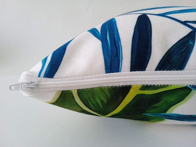 May include: A white pillow with a zipper closure. The pillow has a blue and green tropical leaf pattern.