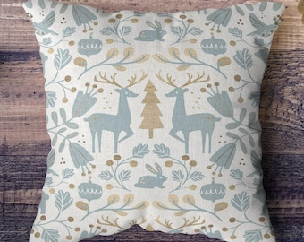 May include: A white throw pillow with a blue and gold pattern of deer, trees, and floral designs. The pillow is made of a soft, textured fabric.