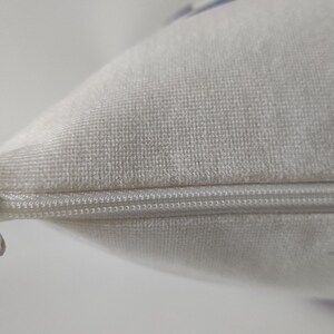 May include: Close-up of a white pillow with a zipper closure. The pillow has a soft, textured surface. The zipper is silver and runs along the edge of the pillow, providing a secure closure for the pillowcase.