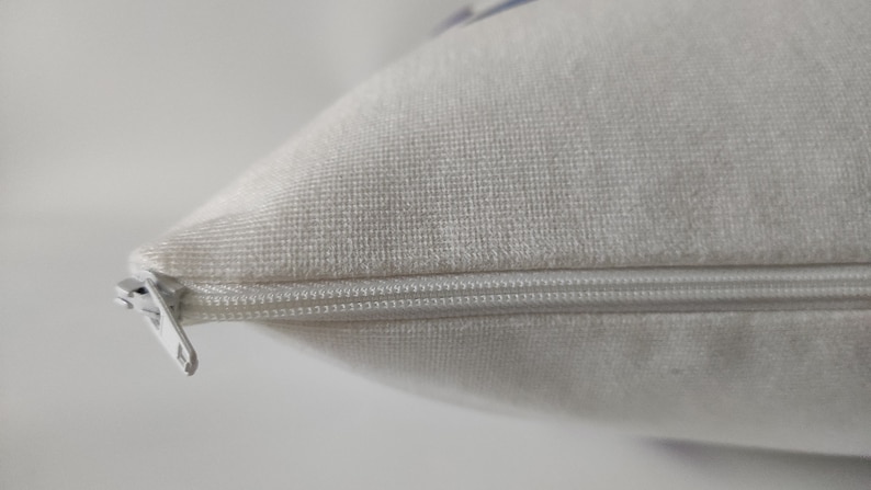 May include: Close-up of a white pillow with a zipper closure. The pillow has a soft, textured surface. The zipper is silver and runs along the edge of the pillow, providing a secure closure for the pillowcase.