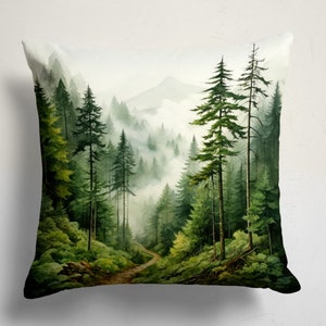 Puede incluir: Un cojín cuadrado con una ilustración impresa de un paisaje forestal denso. La escena muestra árboles de hoja perenne altos, follaje verde exuberante y un sendero de tierra sinuoso que conduce a una cordillera brumosa al fondo.