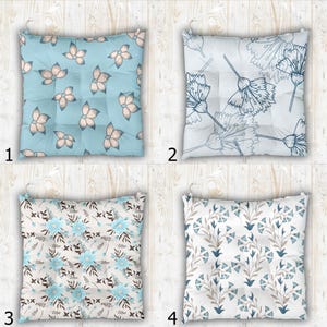 May include: Four square seat cushions with tufted details. Cushion 1 is light blue with beige flower motifs. Cushion 2 is white with dark blue line-art floral patterns. Cushion 3 features light blue flowers and brown leaves. Cushion 4 has blue floral sprigs.