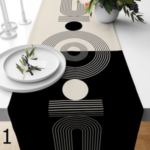 May include: Black and white geometric table runner with a modern design. The runner features circles, arches, and lines.