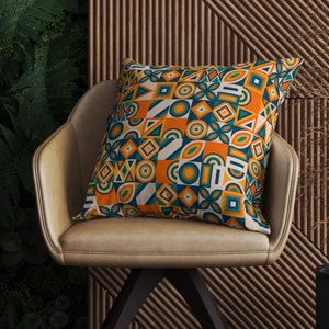 May include: A decorative throw pillow with a geometric pattern in shades of orange, teal, and white. The pillow is sitting on a brown leather chair.