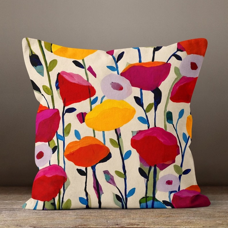 May include: Square throw pillow with a floral design. The pillow features a cream-colored background with colorful flowers in shades of red, pink, orange, and yellow. The flowers have green stems and blue leaves.