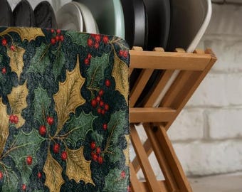 May include: A wooden dish rack with a green and gold patterned tea towel. The towel has a holly leaf and berry design.