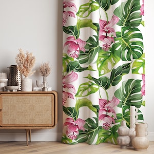 Può includere: Una tenda a tutta altezza caratterizzata da un motivo ripetuto ad acquerello con grandi foglie di monstera verdi e vivaci fiori tropicali rosa su sfondo bianco. Il tessuto cade in morbide pieghe verticali, mostrando un design botanico.