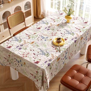Puede incluir: Un mantel rectangular con un estampado floral con flores rojas, moradas, azules y amarillas sobre un fondo blanco. Un jarrón amarillo con flores y un plato pequeño amarillo con un postre están sobre la mesa.