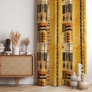 Könnte beinhalten: Gelb-beiger Vorhang mit schwarzen geometrischen Mustern. Der Vorhang hat ein sich wiederholendes Muster aus Rechtecken und vertikalen Streifen. Das Design hat ein afrikanisches Stammes-Thema. Der Vorhang hängt vor einer weißen Wand.