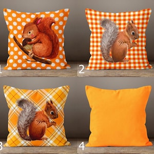 May include: A set of four square throw pillows. Three pillows feature illustrations of brown squirrels on orange backgrounds with white polka dots, orange and white gingham checks, and orange plaid patterns. One pillow is solid orange.